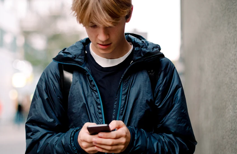 Ung fyr med stor dunjakke og rygsæk, står udenfor med sin mobil