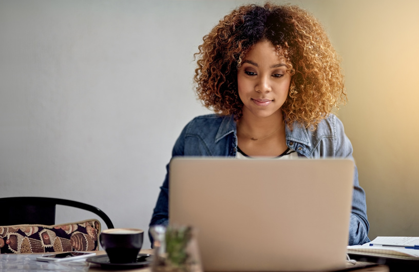 Kvinde med stort krøllet hår, drikker kaffe og sidder ved sin computer
